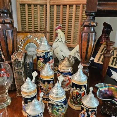 Collection of vintage German-style ceramic beer steins with metal lids, displayed alongside antique washboards, a rooster figurine, and...