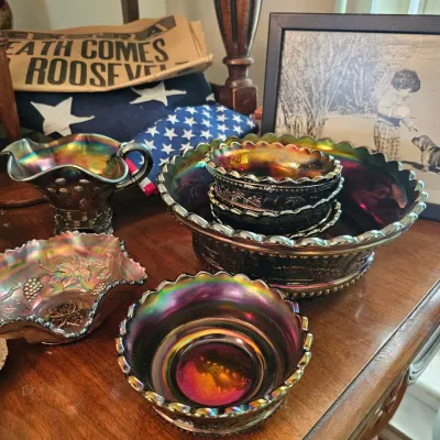 Assortment of vintage amethyst carnival glass tableware, including ruffled bowls and a small pitcher, displayed alongside a framed...
