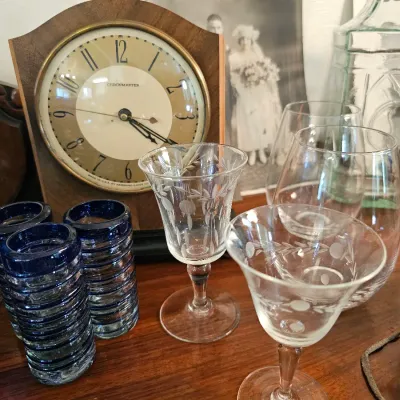 Vintage Chronmaster mantel clock with a wooden case, displayed alongside etched crystal stemware and ribbed blue-rimmed shot glasses.