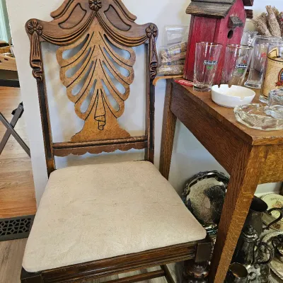 Vintage wooden dining chair featuring an ornate carved splat back with a stylized leaf or fan motif, turned front legs, and a neutral...