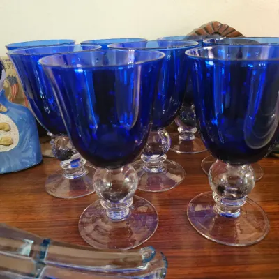 Set of cobalt blue water goblets featuring clear glass stems with a ball detail, displayed alongside vintage decorative items.