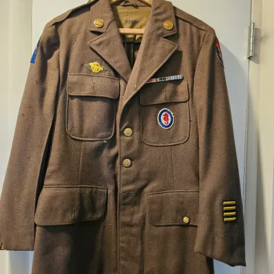 Vintage World War II era US Army olive drab wool service coat, featuring various insignia, patches, and service stripes.