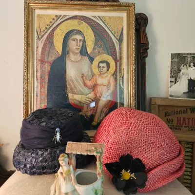 Vintage women's hats, including a dark woven straw hat with a bug brooch and a pink woven straw hat with a black flower accent,...