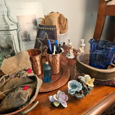 Assorted vintage collectibles including hammered copper cups, a blue glass pitcher, beaded leather pouches, and small porcelain floral...