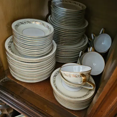 Vintage fine china dinnerware set featuring a delicate gold leaf pattern and gold-trimmed rims, including stacks of plates, bowls, and...