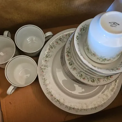 Noritake fine china dinnerware set in a cardboard box, featuring a delicate floral pattern with silver trim, including plates, saucers,...