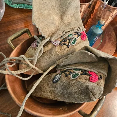 Pair of vintage Native American style beaded leather moccasins with floral beadwork, displayed inside a copper bowl.