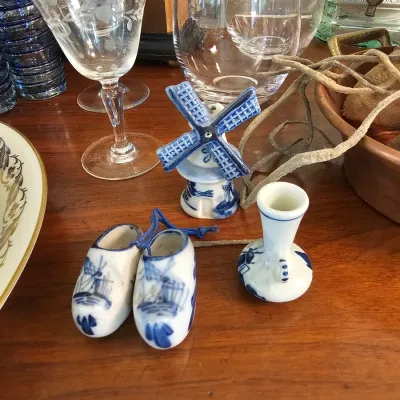 Delft Blue style miniature porcelain souvenirs, including a pair of wooden shoes, a windmill, and a small vase, displayed alongside...