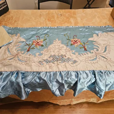 Vintage light blue satin bed runner or valance featuring intricate cream applique, floral embroidery, and a ruffled border.