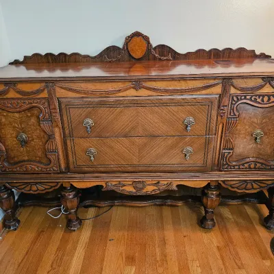 Antique Jacobean Revival style wooden sideboard featuring ornate carvings, burl wood veneers, two central drawers, flanking cabinets, and...