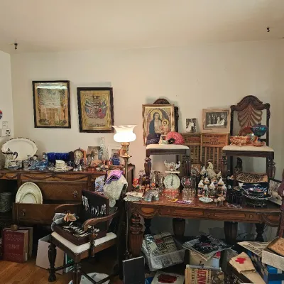 Assorted vintage collectibles, glassware, and antique furniture, including a wooden buffet, carved chairs, framed artwork, and a vanity...