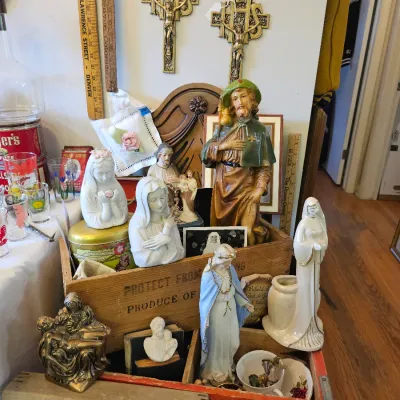 Collection of religious figurines, including depictions of the Virgin Mary, Jesus, and various saints, displayed alongside vintage wooden...