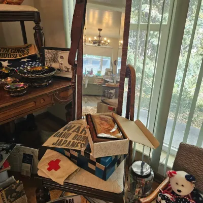Vintage wooden cheval mirror and matching chair displaying World War II memorabilia, including a Pearl Harbor Life magazine, historical...