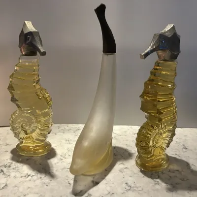 Sale Photo Thumbnail #13: Vintage Avon novelty cologne bottles, featuring two glass seahorses with silver-toned caps and one frosted glass dolphin with a black cap.