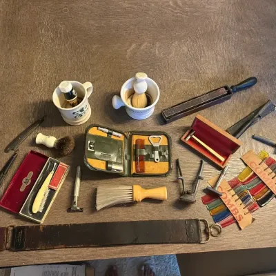 Sale Photo Thumbnail #72: Collection of vintage shaving accessories, including straight razors, safety razors, shaving mugs, brushes, a leather strop, and a card of colorful combs.
