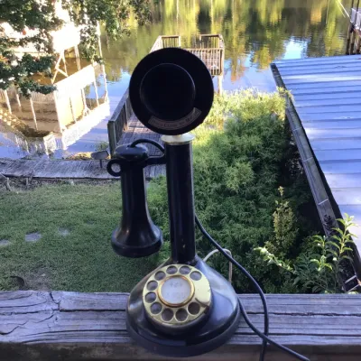 Sale Photo Thumbnail #82: Vintage black candlestick telephone with a rotary dial and brass accents, showing some wear consistent with age.