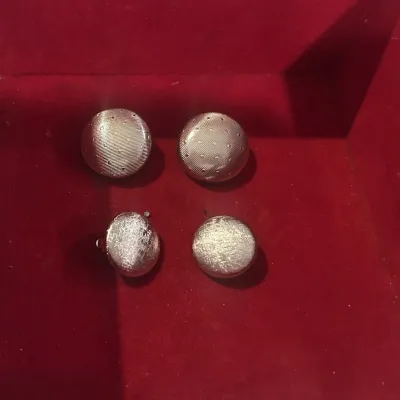 Sale Photo Thumbnail #25: Two pairs of vintage silver-tone clip-on earrings, including one pair with a textured polka dot pattern and one pair with a brushed satin finish, displayed on a red velvet surface.