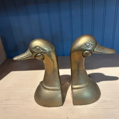 Sale Photo Thumbnail #167: Pair of vintage solid brass duck head bookends, showing a warm patina and classic mid-century style.