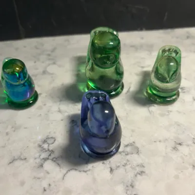 Sale Photo Thumbnail #55: Collection of four vintage glass bird figurines, including three in shades of green and one in blue, displayed on a marble surface.