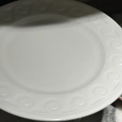 White ceramic plate featuring an embossed scroll pattern along the rim, shown in clean condition.