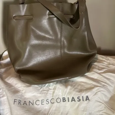 Sale Photo Thumbnail #101: Francesco Biasia taupe leather bucket bag with shoulder strap, resting on its branded white dust bag.