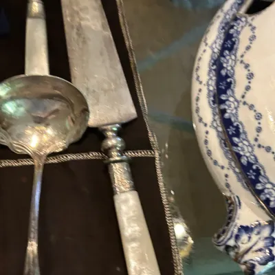 Vintage silver-plated serving pieces, including a ladle and a cake server with a mother-of-pearl handle, shown alongside a blue and white...