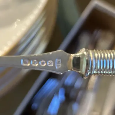 Close-up of hallmarks stamped on a silver-plated or sterling silver flatware handle, showing maker's marks and purity symbols.