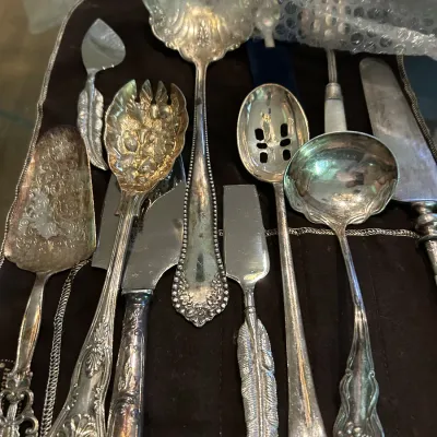 Assortment of vintage silver-plated serving utensils, including ladles, a pie server, and a slotted spoon, showing some tarnish.