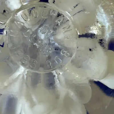 Close-up of the maker's mark on a Maude and St. Clair art glass paperweight, showing the embossed signature on the base.