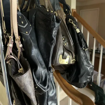 Sale Photo Thumbnail #103: Collection of designer and leather handbags, including black and brown shoulder bags, hanging from a metal rack.