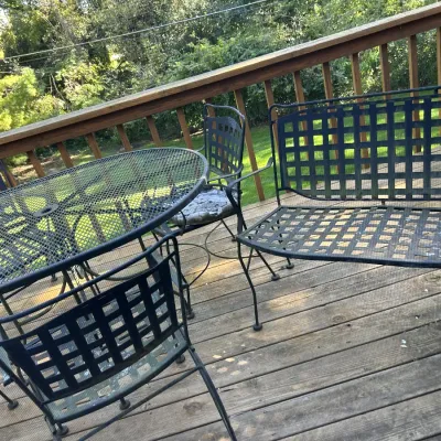 Black wrought iron patio furniture set, including a mesh-top round table, a matching bench, and several chairs with a grid-pattern...