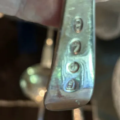 Close-up of hallmarks on a vintage sterling silver spoon handle, showing a series of four stamped maker's and purity marks.