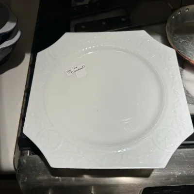 Set of seven white octagonal ceramic plates featuring embossed floral and vine borders, with one plate noted as damaged.