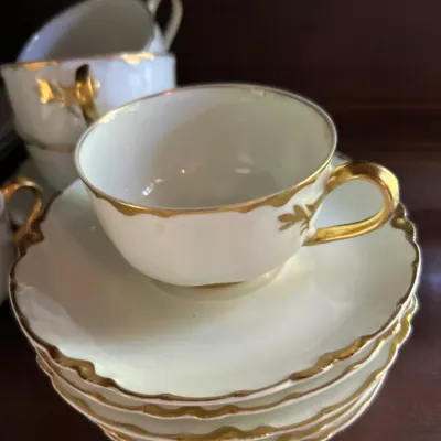 Vintage white porcelain teacup and saucer set featuring scalloped edges and elegant gold-gilded trim and handles.
