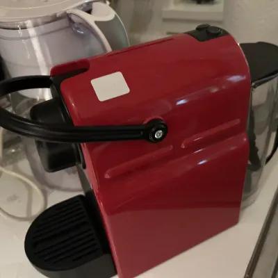 Nespresso Inissia espresso machine in cherry red, featuring a compact design with a black locking handle and water reservoir.