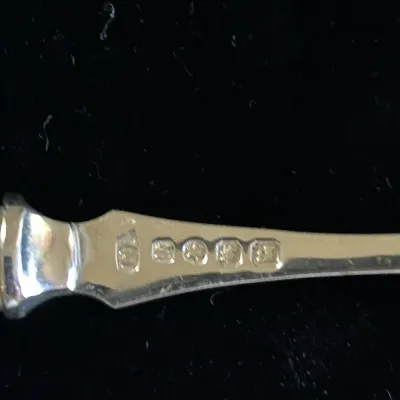 Close-up of hallmarks stamped on the handle of a silver flatware piece, set against a black background.