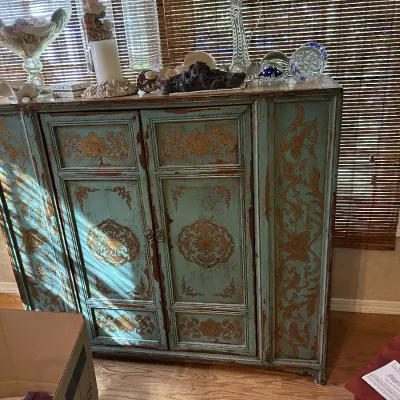 Distressed teal and gold painted cabinet with ornate floral scrollwork, featuring a two-door center compartment and flanking side panels.
