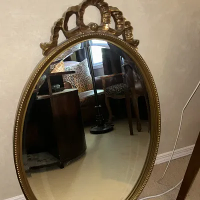 Sale Photo Thumbnail #112: Vintage oval wall mirror featuring a beaded gold-painted frame and an ornate decorative crest at the top.