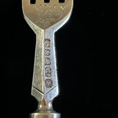 Close-up of a silver-plated fork showing a grape cluster engraving and maker's hallmarks on the neck.