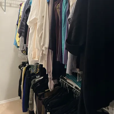 Assorted women's clothing hanging on two tiers of wire closet shelving.