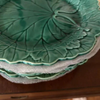 Stack of vintage Bordallo Pinheiro green cabbage leaf majolica plates, separated by protective foam padding.