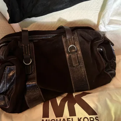Michael Kors dark brown suede and leather duffle bag, resting on its original branded dust bag.