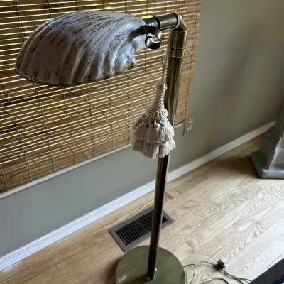 Vintage brass floor lamp featuring a ceramic clamshell-style shade with gold accents and a decorative hanging tassel.