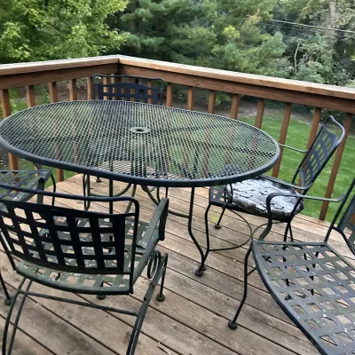 Wrought iron patio dining set featuring an oval mesh-top table with an umbrella hole and matching lattice-back chairs.