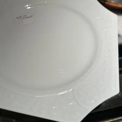 Vintage white milk glass plate featuring an octagonal rim with embossed floral and leaf motifs, marked as part of a set of seven.