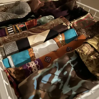 Collection of vintage patterned silk and fabric scarves neatly rolled and organized in a white wire drawer basket.