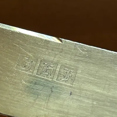 Close-up of a silver-plated or pewter item showing three stamped hallmarks on a scratched metal surface.