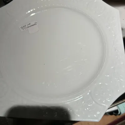 Vintage white milk glass plate, part of a set of seven, featuring an embossed floral and geometric border design.