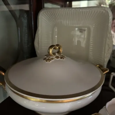 Vintage white porcelain covered serving dish with gold trim and a decorative gold handle, displayed alongside a square cream-colored...