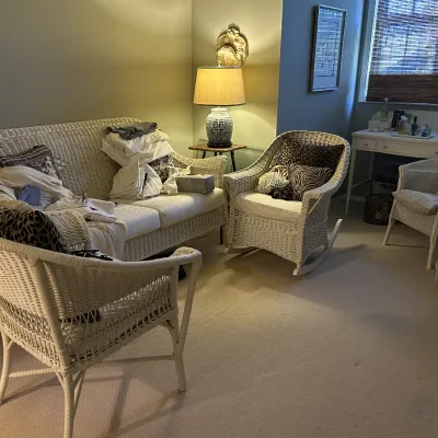 Sale Photo Thumbnail #107: White wicker living room set including a sofa, rocking chair, two armchairs, and a matching side table, paired with a white wooden writing desk in the background.